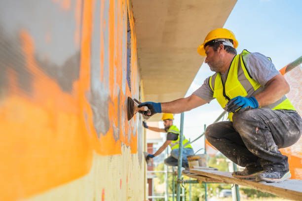 Workers applying orange coating to an exterior wall from scaffolding