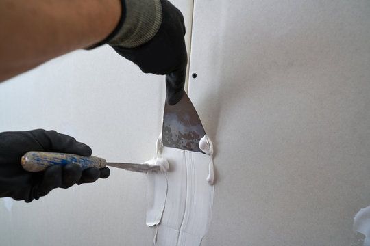 Two taping knives applying joint compound to a drywall seam
