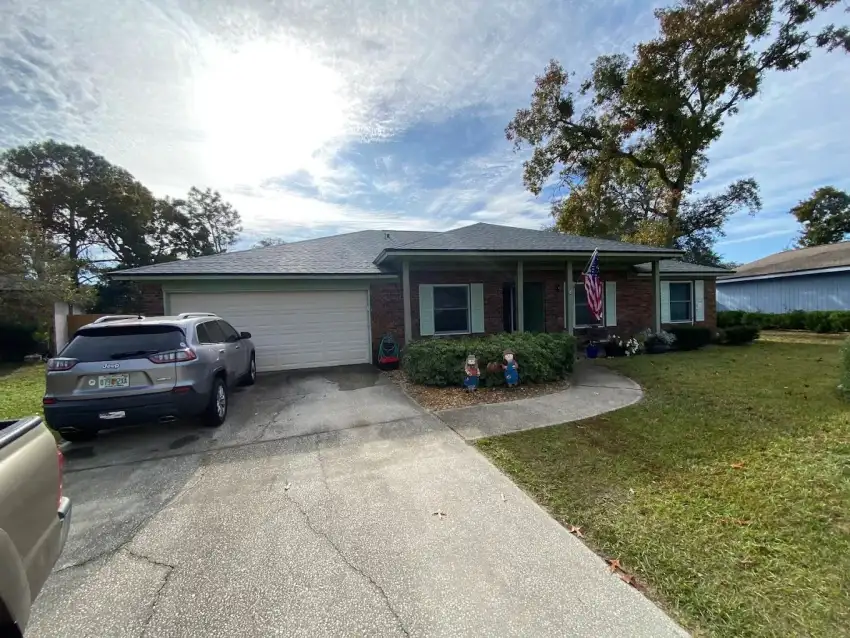 Single-story brick home with muted green trim and shutters viewed from the driveway