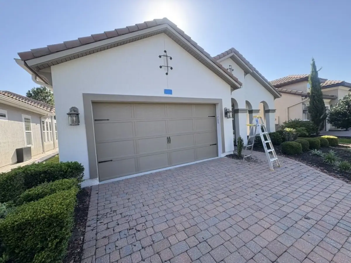 Textured home exterior before painting, showing the garage and front entry with a ladder in the driveway